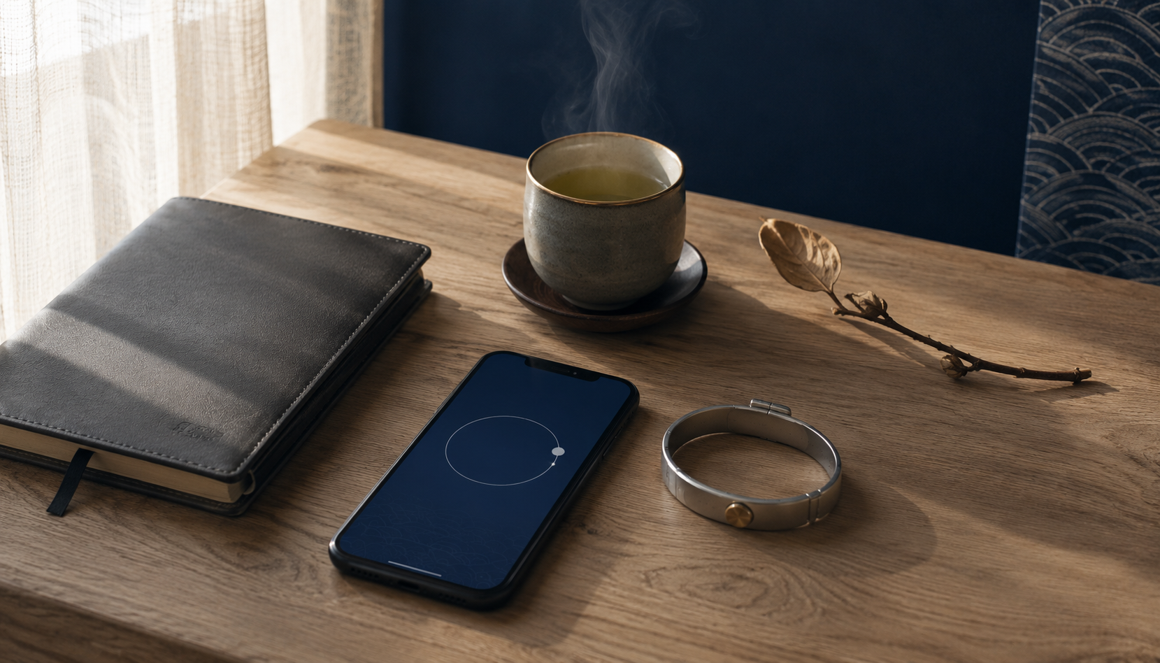 A quiet morning still-life on a wood desk: a leather notebook, a ceramic cup of tea with rising steam, a smartphone showing a soft abstract indigo home screen, a wristband, and a small dried branch.